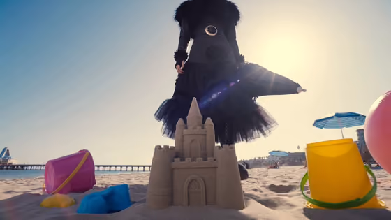 Gothic Woman Crushes Sandcastle on Bright Beach